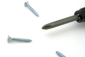 A detailed view of a screwdriver with screws scattered on a white surface, ideal for tool or maintenance themes.